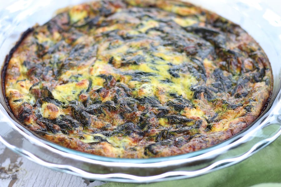 Spinach Quiche in a clear pie plate with a scalloped edge.