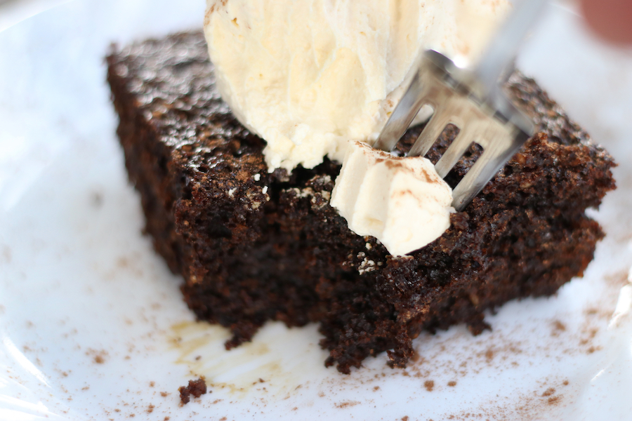 A fork diving into a slice of Irish Molasses Cake that is topped with whipped cream.