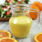 Freshly made Orange Salad Dressing in a clear glass jar, surrounded by vibrant orange slices.