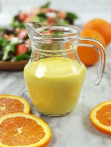 Orange Vinaigrette in a small clear glass pitcher sitting on a marble countertop.