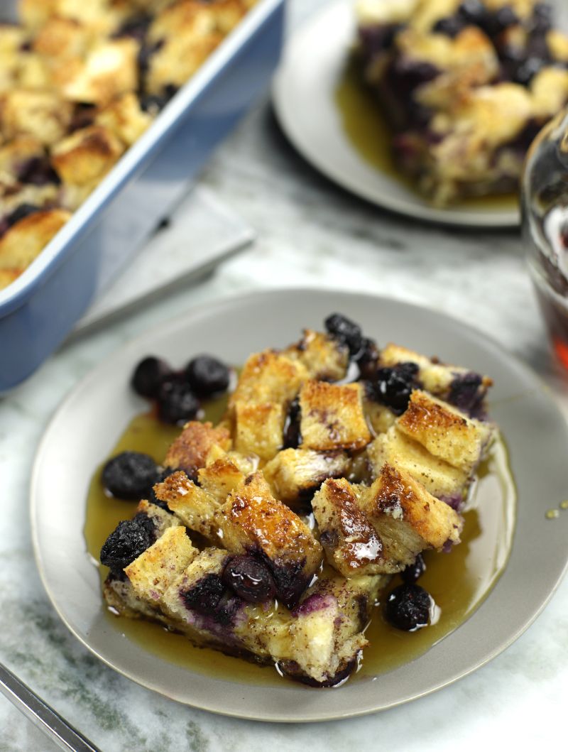 A slice of Sourdough French Toast Casserole baked with blueberries and covered with maple syrup.