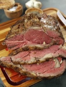 A Standing Rib Roast cut with three slices sitting on a wooden cutting board.