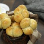 Golden dinner rolls, perfectly baked in muffin tins, nestled in a basket alongside a butter dish and cozy hot pads.